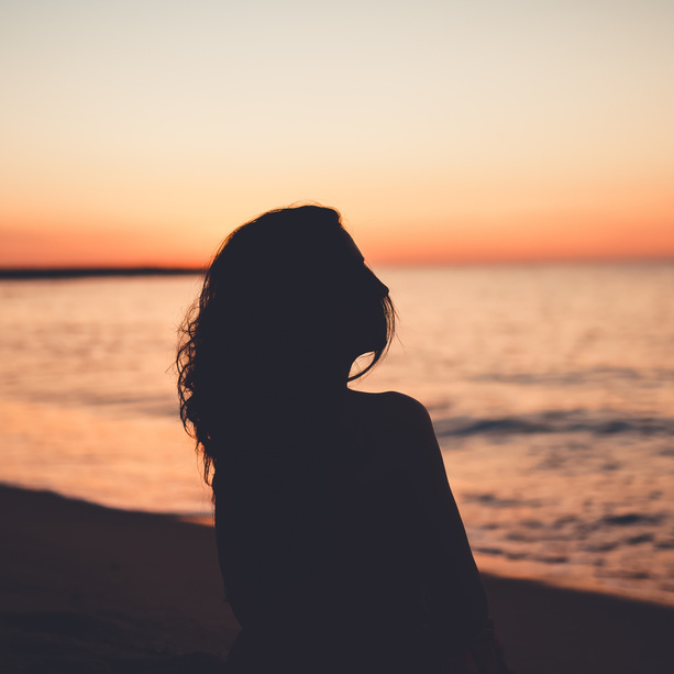 Anonymous woman on seashore at sunset